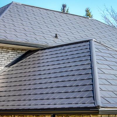 Close-up of a house roof featuring dark, overlapping solar roof tiles under a clear blue sky.