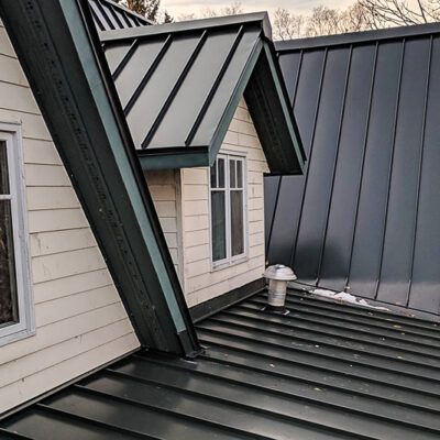 A dormer window with cream-colored siding and a dark standing seam metal roof on a residential house.