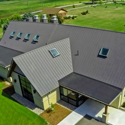An elevated view of a building with a dark metal roof, multiple skylights, and a stone facade on a sunny day.