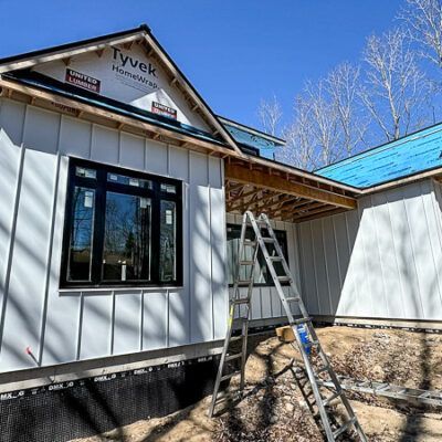 A house under construction with white vertical siding, black-framed windows, and a silver ladder leaning against it.