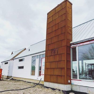 A modern house under construction, featuring a prominent, rust-colored, rectangular metal chimney exterior.