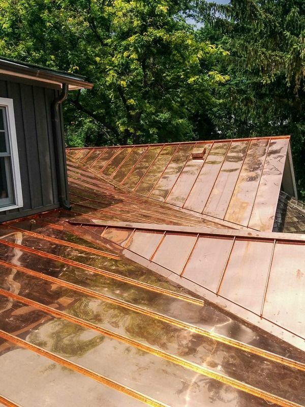 A high-angle view of a new, shiny copper roof with standing seams, transitioning to older, weathered copper panels.