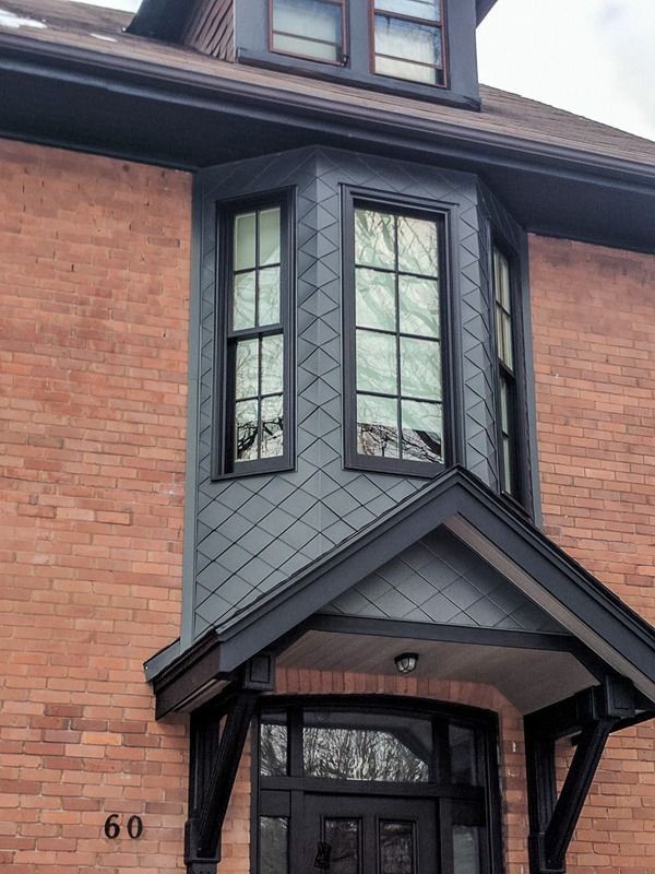 A close-up of a brick house featuring a dark-framed bay window with diamond-patterned siding above the front entryway.