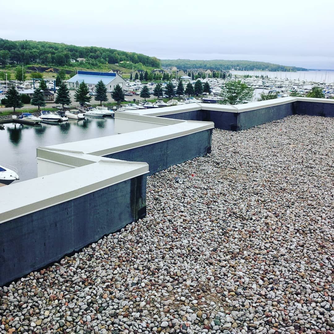 A gravel-covered flat roof with a zigzagging parapet wall overlooking a harbor filled with boats.