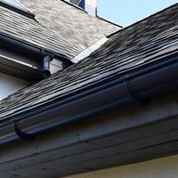 A low-angle view of a grey shingled roof with dark gutters and a metal flashing valley against a clear blue sky.