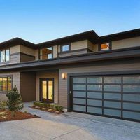A two-story modern house with horizontal brown siding, a glass-paneled garage door, and a front entry under a porch.