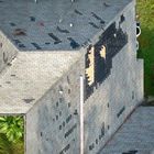 Aerial view of a damaged roof with missing shingles, exposing the underlying wooden deck in a large patch.