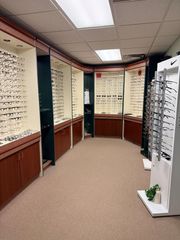 Interior of an eyewear store with glasses displayed on wall-mounted panels and a white sunglasses stand.