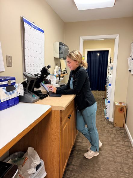 Woman working at a front desk in a small office hallway, typing at a computer.