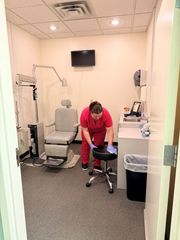 Person in red scrubs adjusting a stool in a small medical exam room.