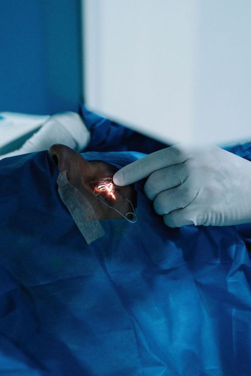 Gloved hand examining a small lit wound on a blue surgical drape