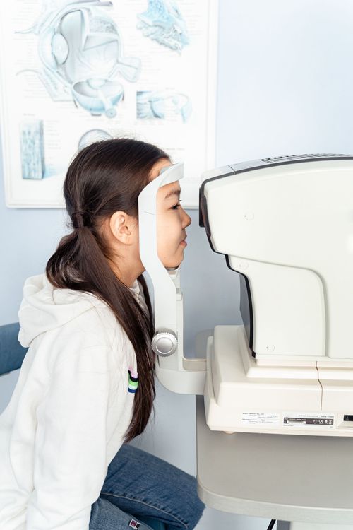 Person seated at an eye exam machine, looking through the viewfinder in a clinic.
