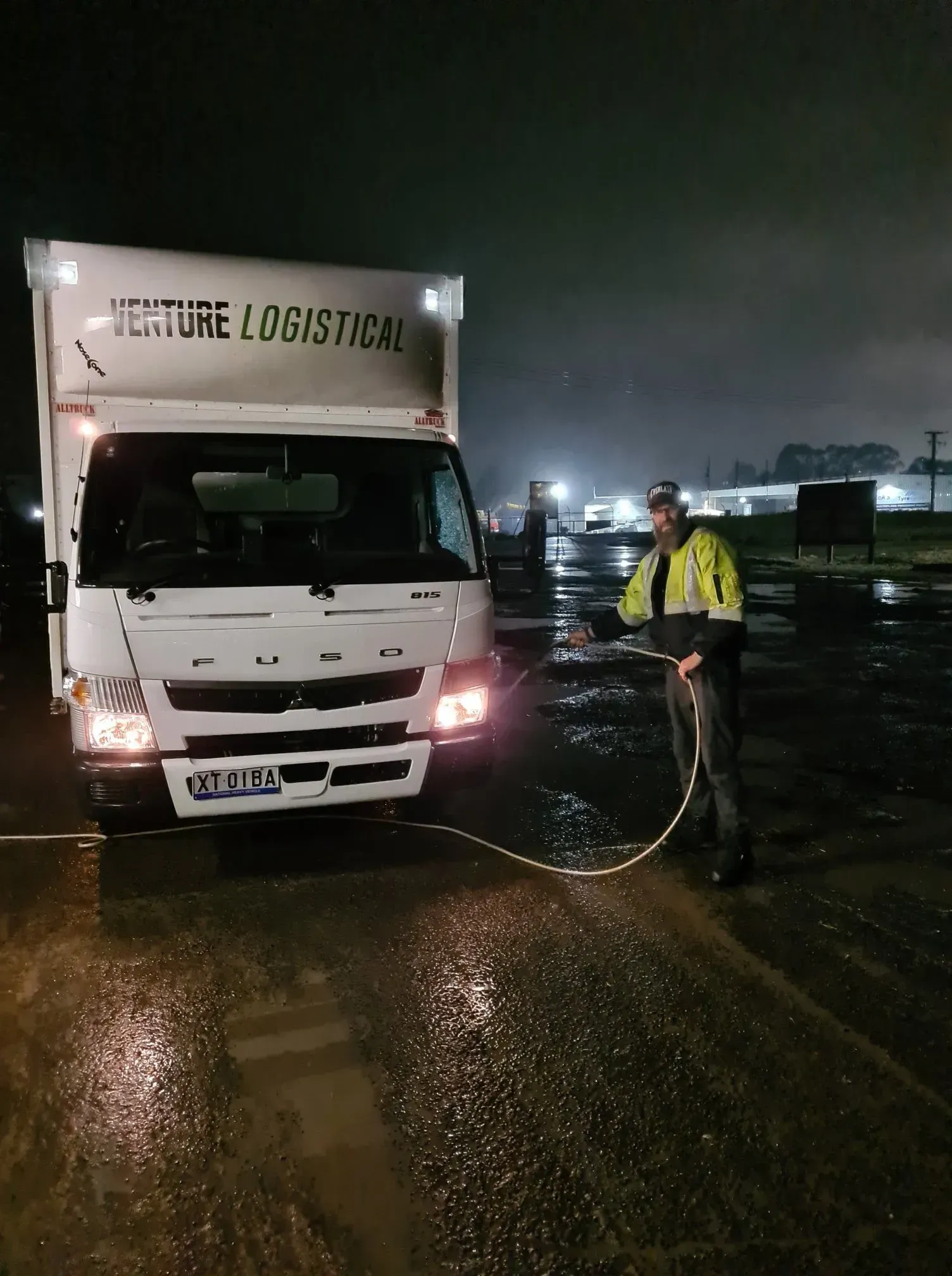 Truck at night in the rain with a worker in a hi-vis jacket standing beside it Truck at night in the rain with a worker in a hi-vis jacket standing beside it