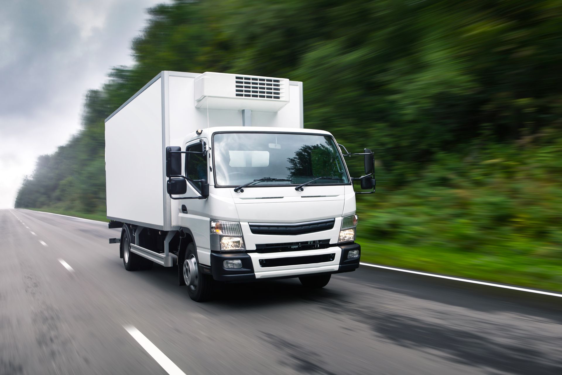 White box truck driving on a wet road beside blurred green trees White box truck driving on a wet road beside blurred green trees