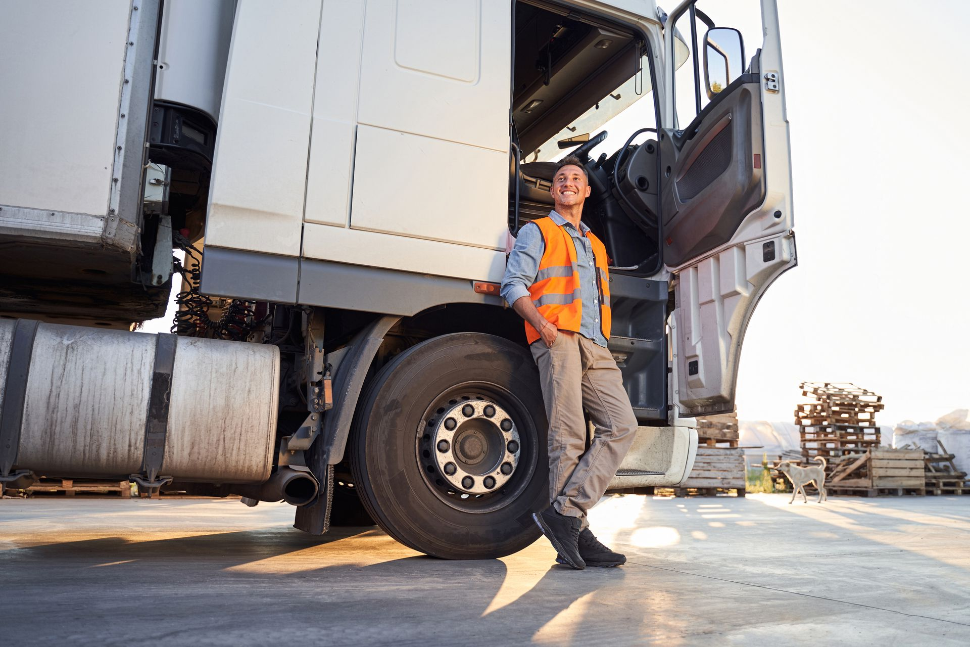 Worker in orange safety vest standing by a large truck in an industrial yard