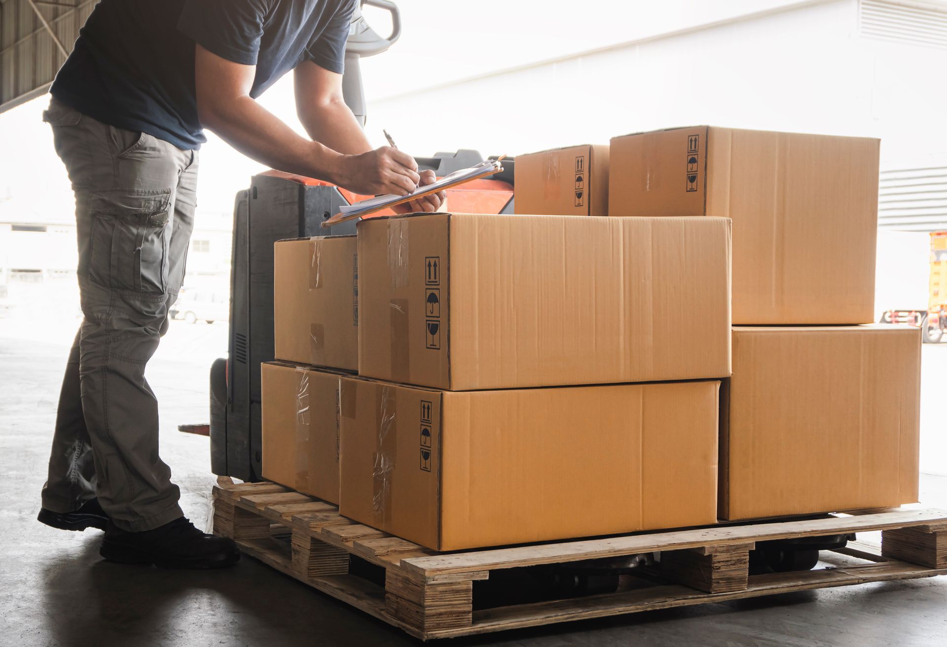 Person loading cardboard boxes onto a pallet in a warehouse or loading area Person loading cardboard boxes onto a pallet in a warehouse or loading area