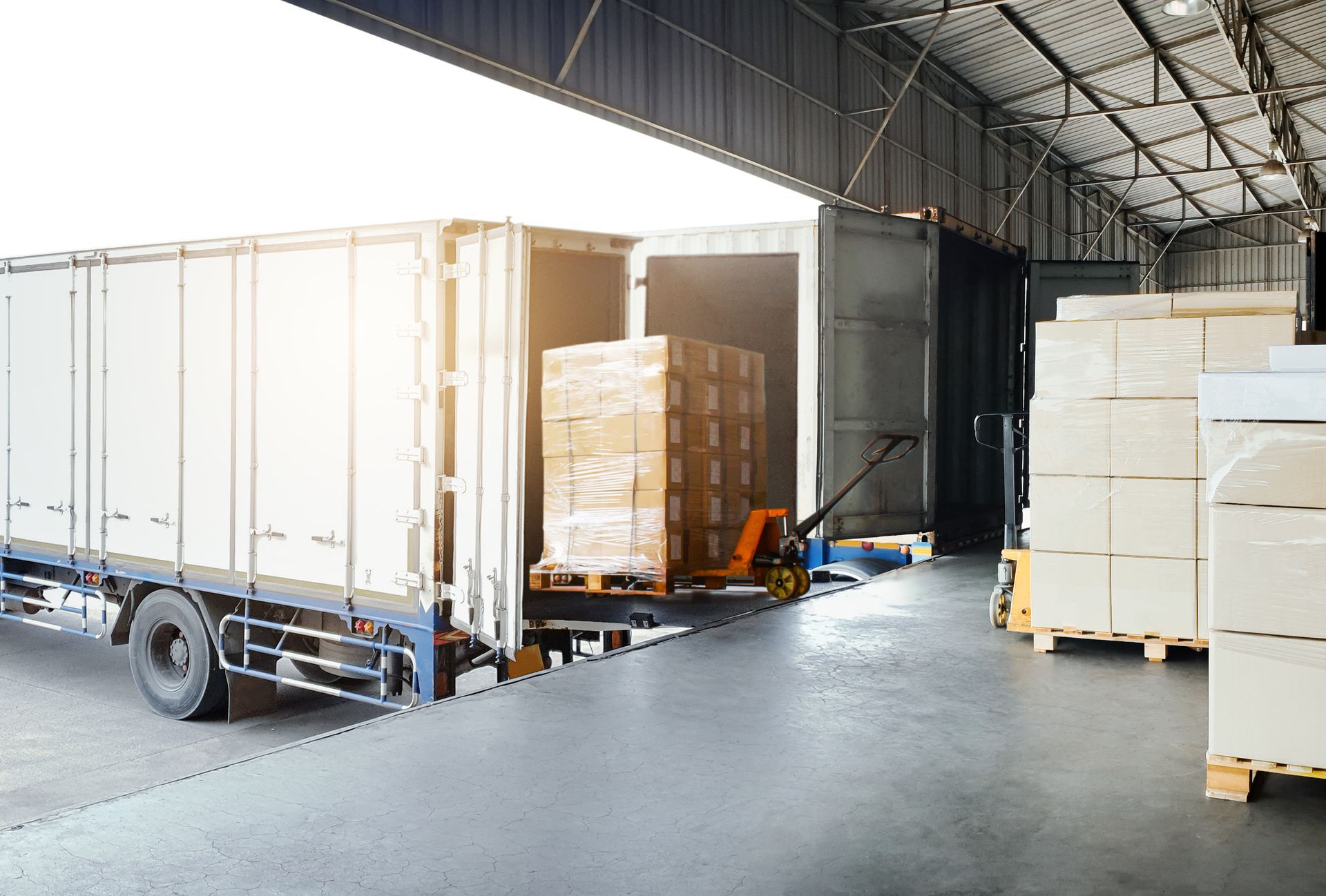 Warehouse loading dock with pallets of boxes and a white truck trailer under a high metal roof Warehouse loading dock with pallets of boxes and a white truck trailer under a high metal roof