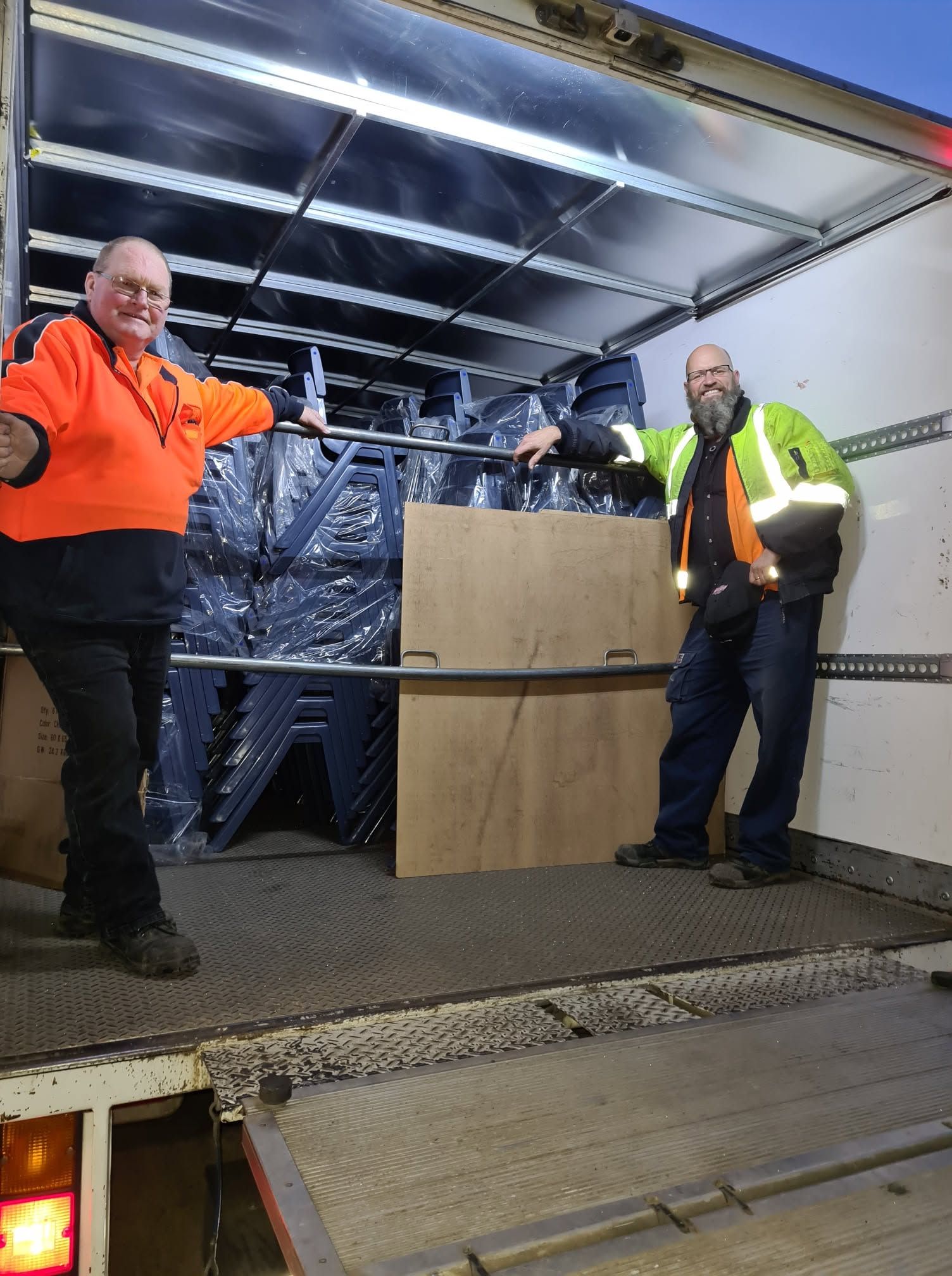 Forklift unloading stacked cardboard boxes from a flatbed truck beside a blue warehouse Forklift unloading stacked cardboard boxes from a flatbed truck beside a blue warehouse
