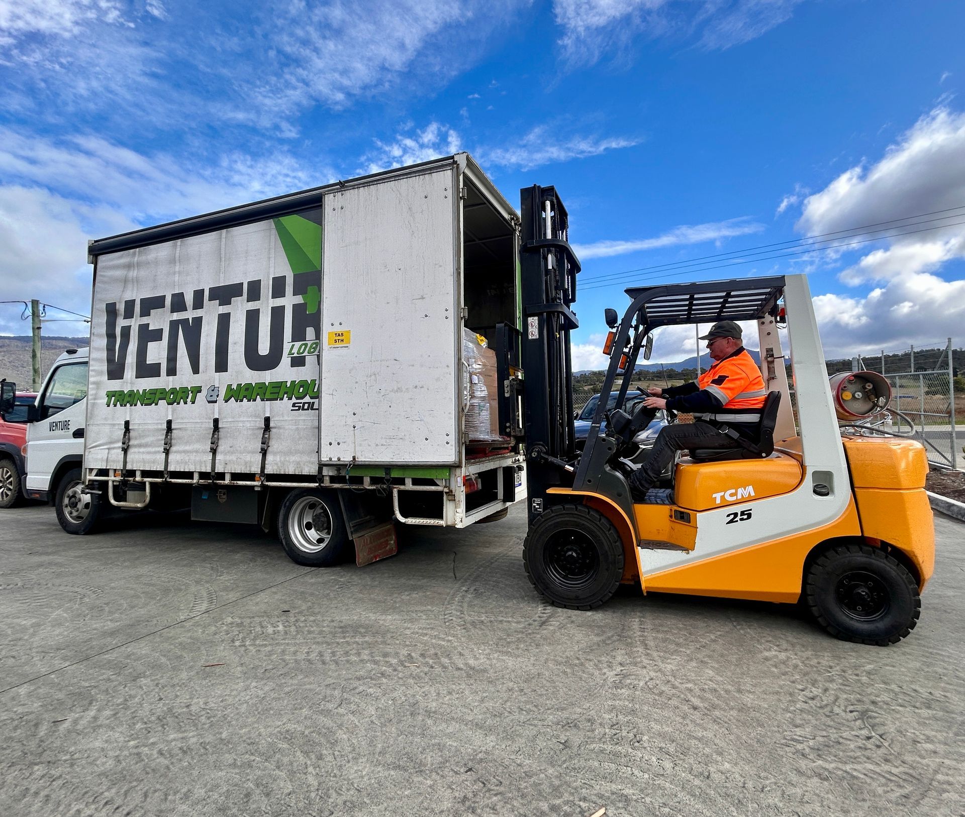 Forklift loading a Venturi truck in a gravel yard under a blue sky