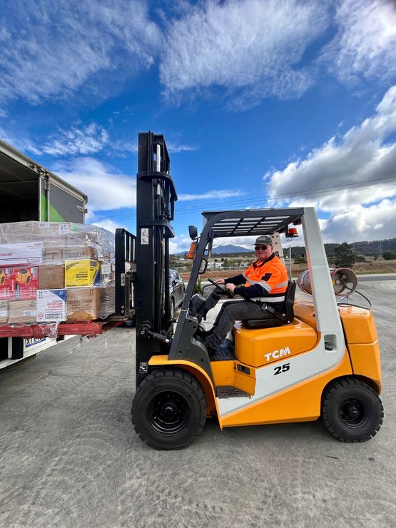 Venture Real Tasmanian Operations ad with forklift driver in orange gear, warehouse yard background, freight and winery logistics Venture Real Tasmanian Operations ad with forklift driver in orange gear, warehouse yard background, freight and winery logistics