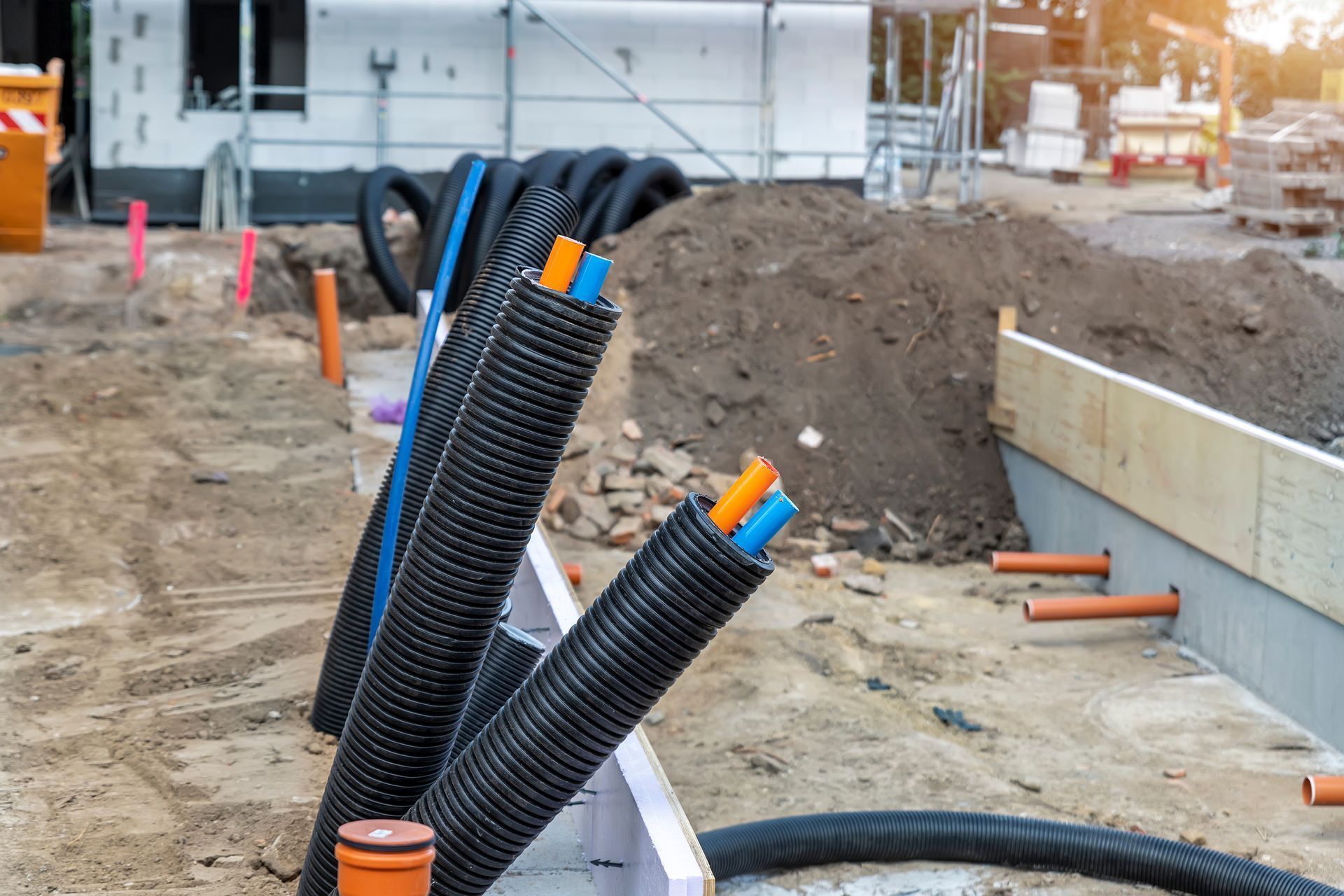 Construction site with black utility conduits and orange-capped pipes near a dirt trench