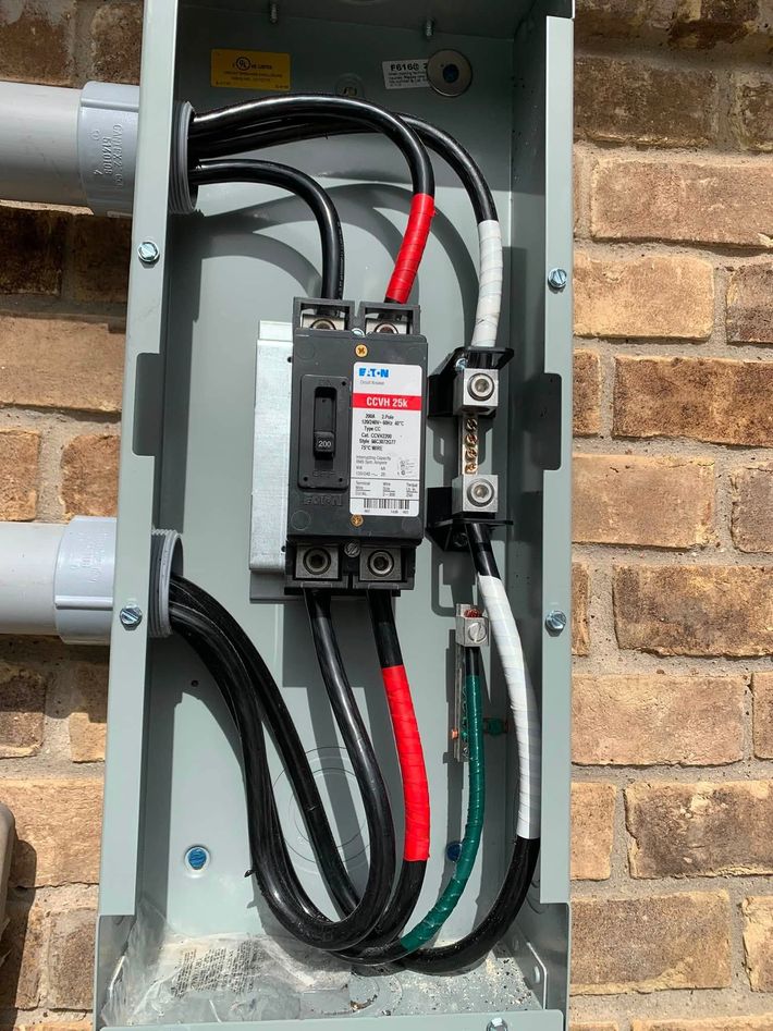 Open electrical breaker panel with black and red wires in a gray metal box against a brick wall