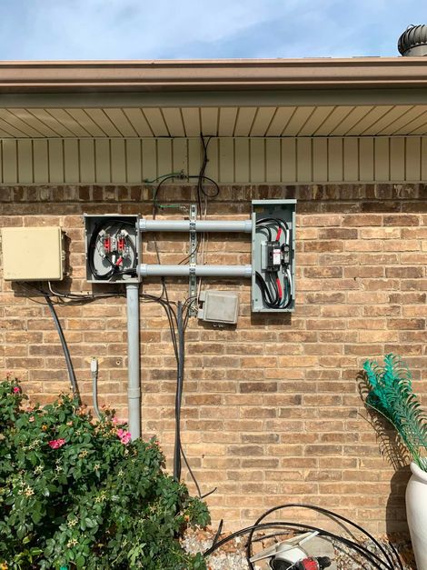 Brick house exterior with two open electrical panels and exposed wiring under the roof eave