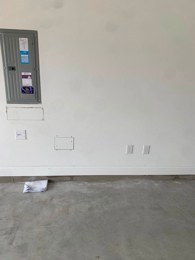 Empty room with gray walls, exposed electrical panel, outlets, and bare concrete floor