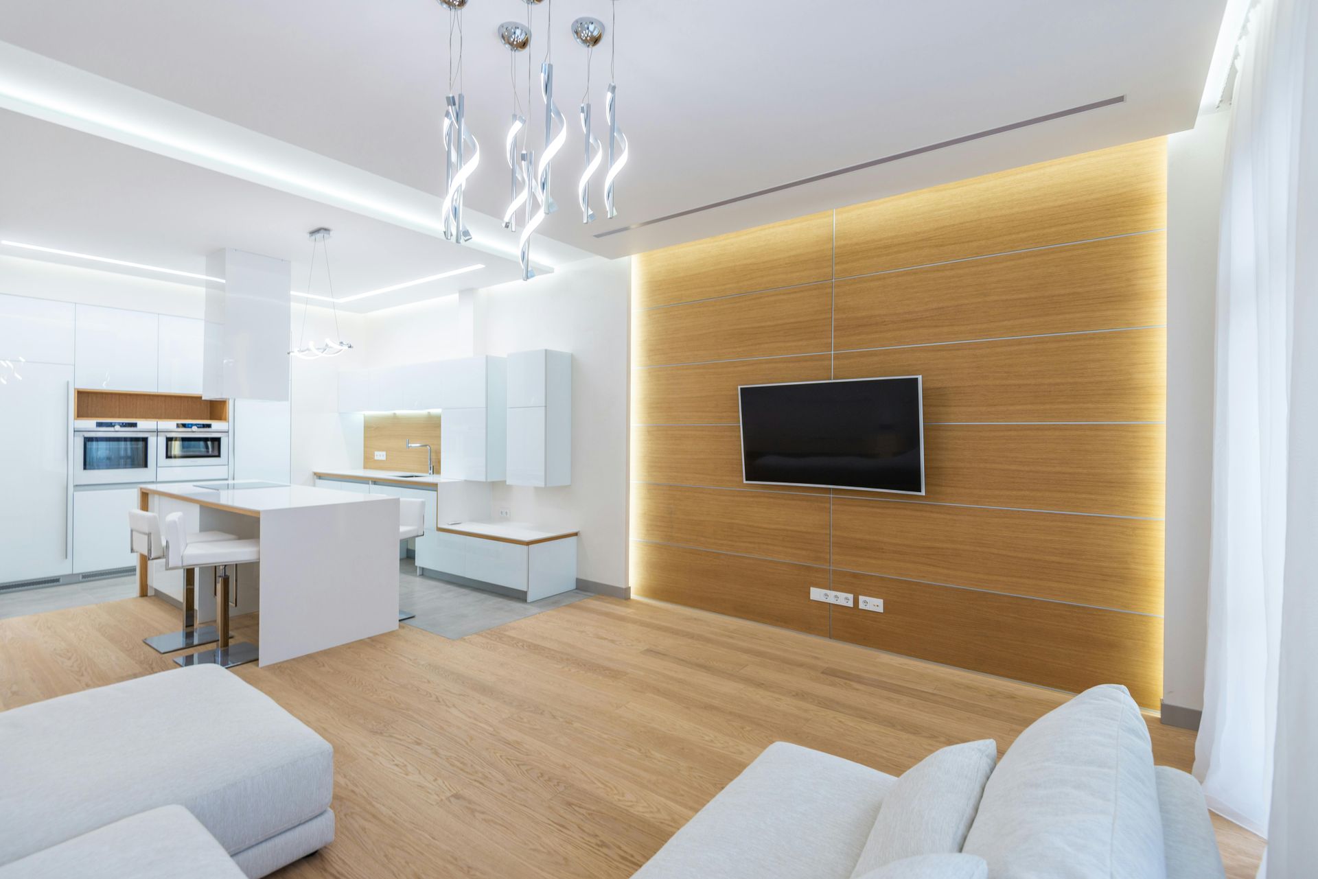Modern open-plan living room and kitchen with white furniture, wood accent wall, and wall-mounted TV