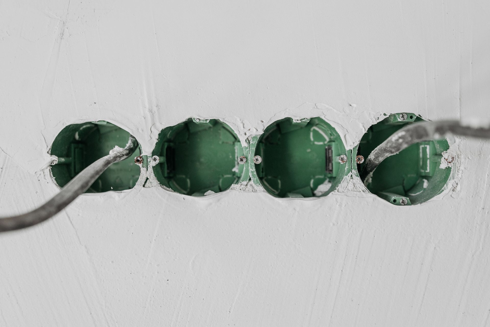 Four green electrical boxes set in a white wall with cables running through them