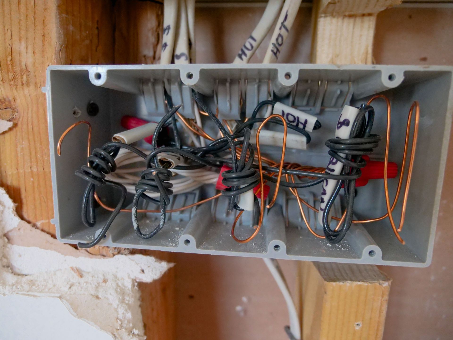 Open electrical junction box with tangled wires and cable bundles in a wall cavity