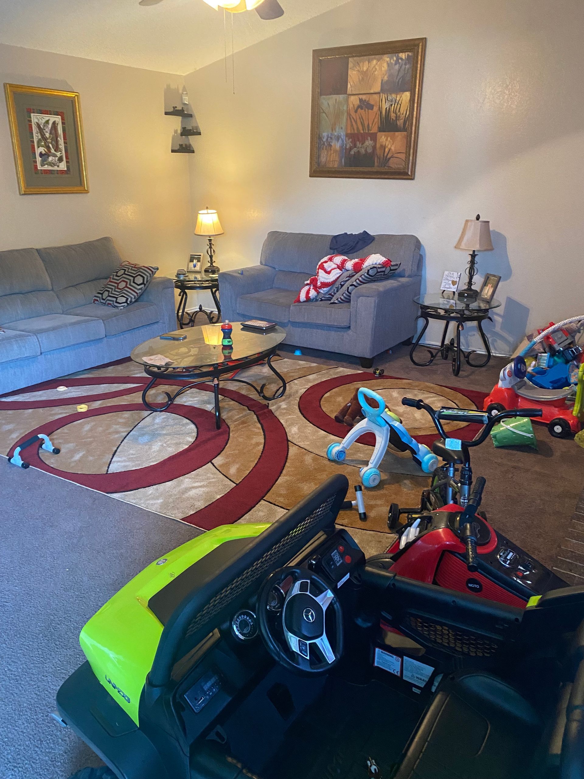 Living room with a gray sofa, rug, and children's ride-on toys.