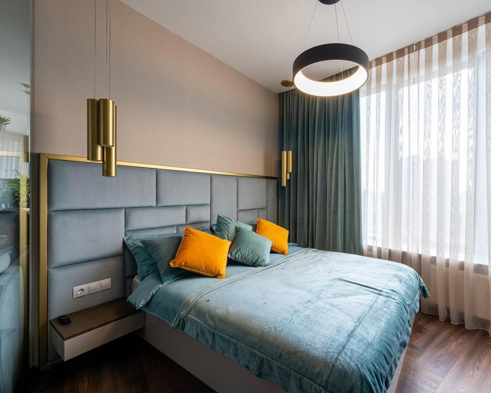 Bedroom with bed, blue headboard, gold accents, and window with teal curtains.