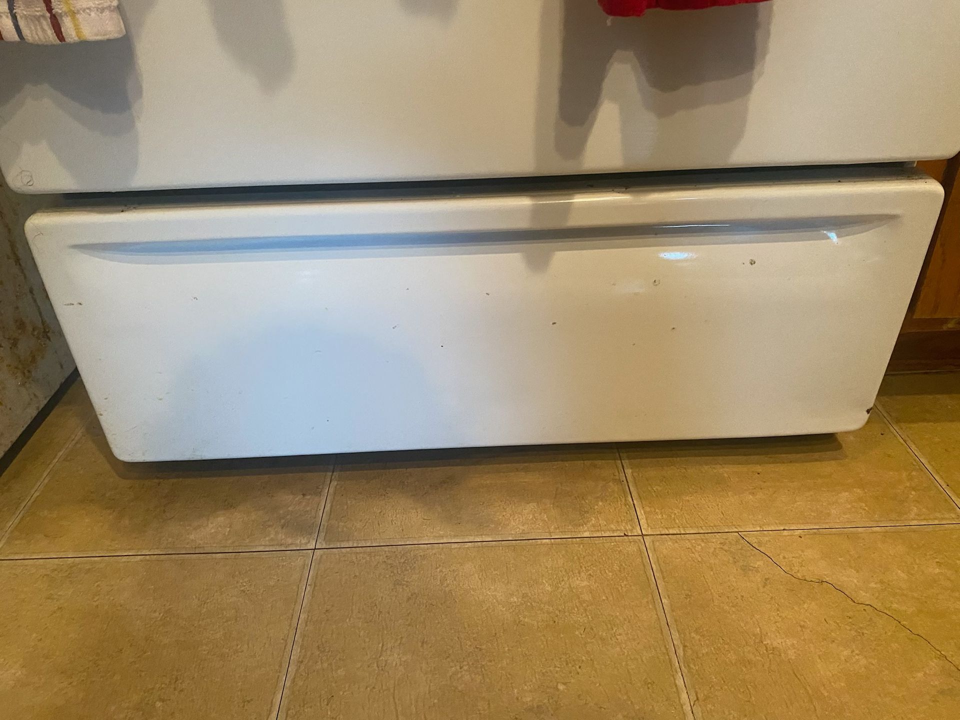 White refrigerator bottom drawer on a tiled floor.