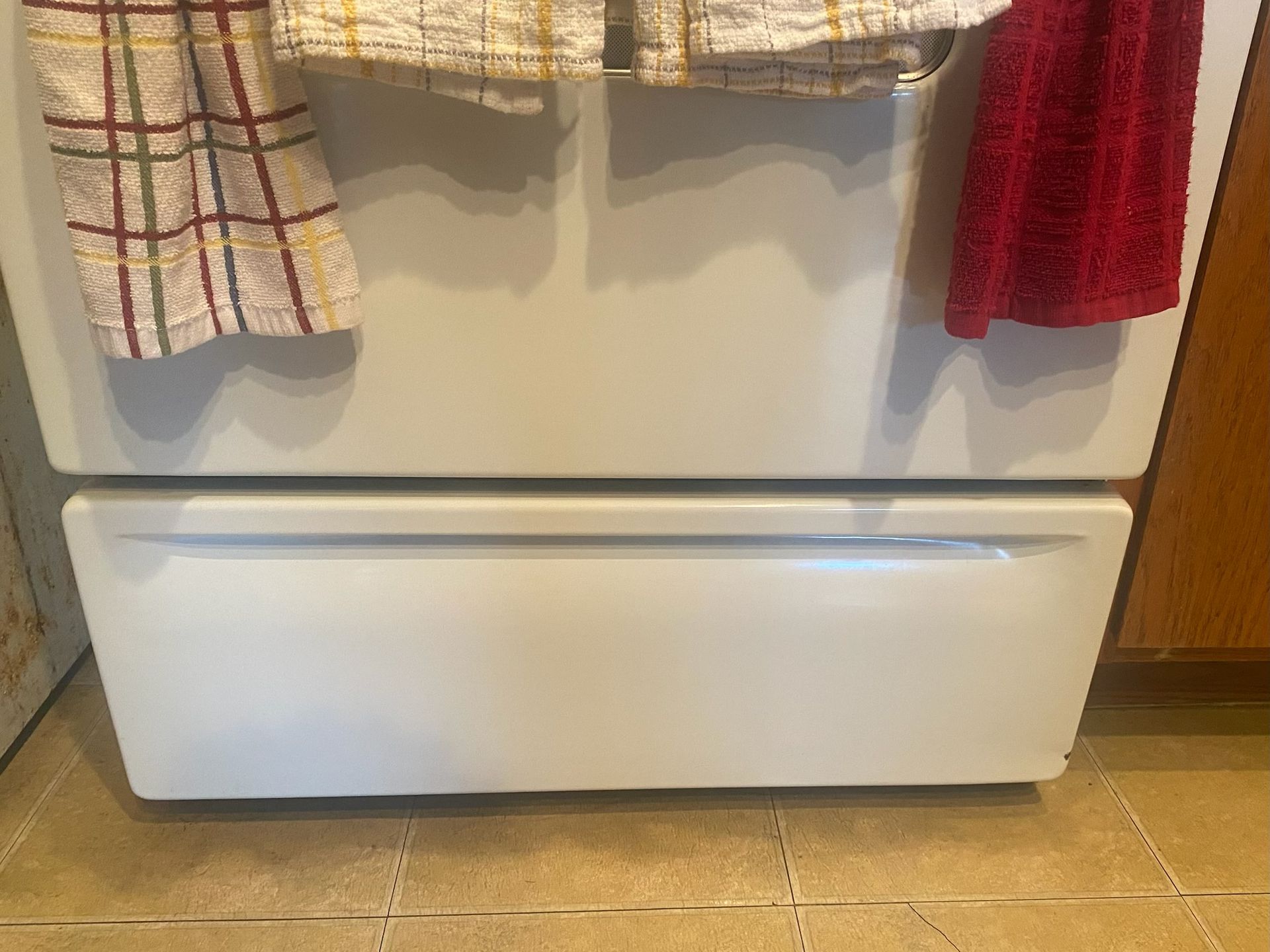 White refrigerator with a drawer, two dish towels hanging from the top.