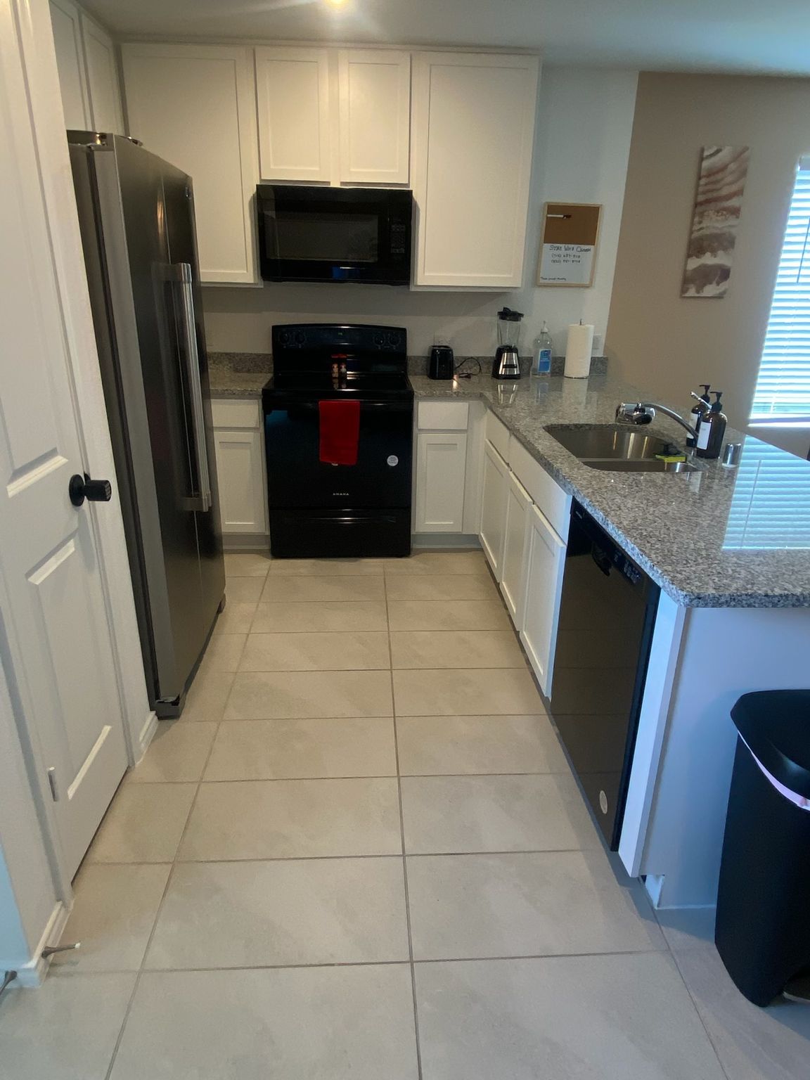 Small kitchen with stainless fridge, black stove, white cabinets, and granite countertops.