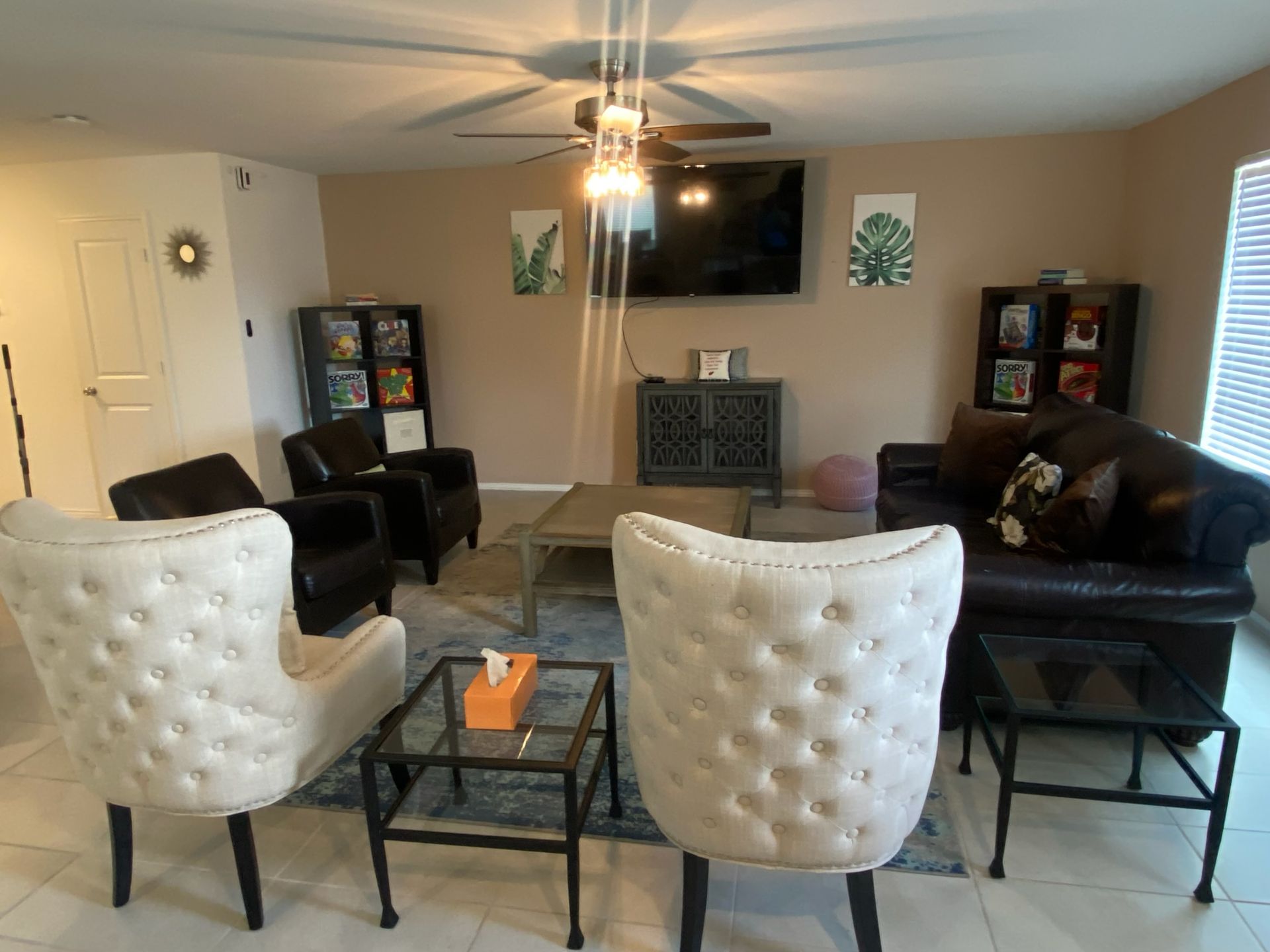 Living room with two tufted chairs, black sofas, TV, fireplace, and ceiling fan