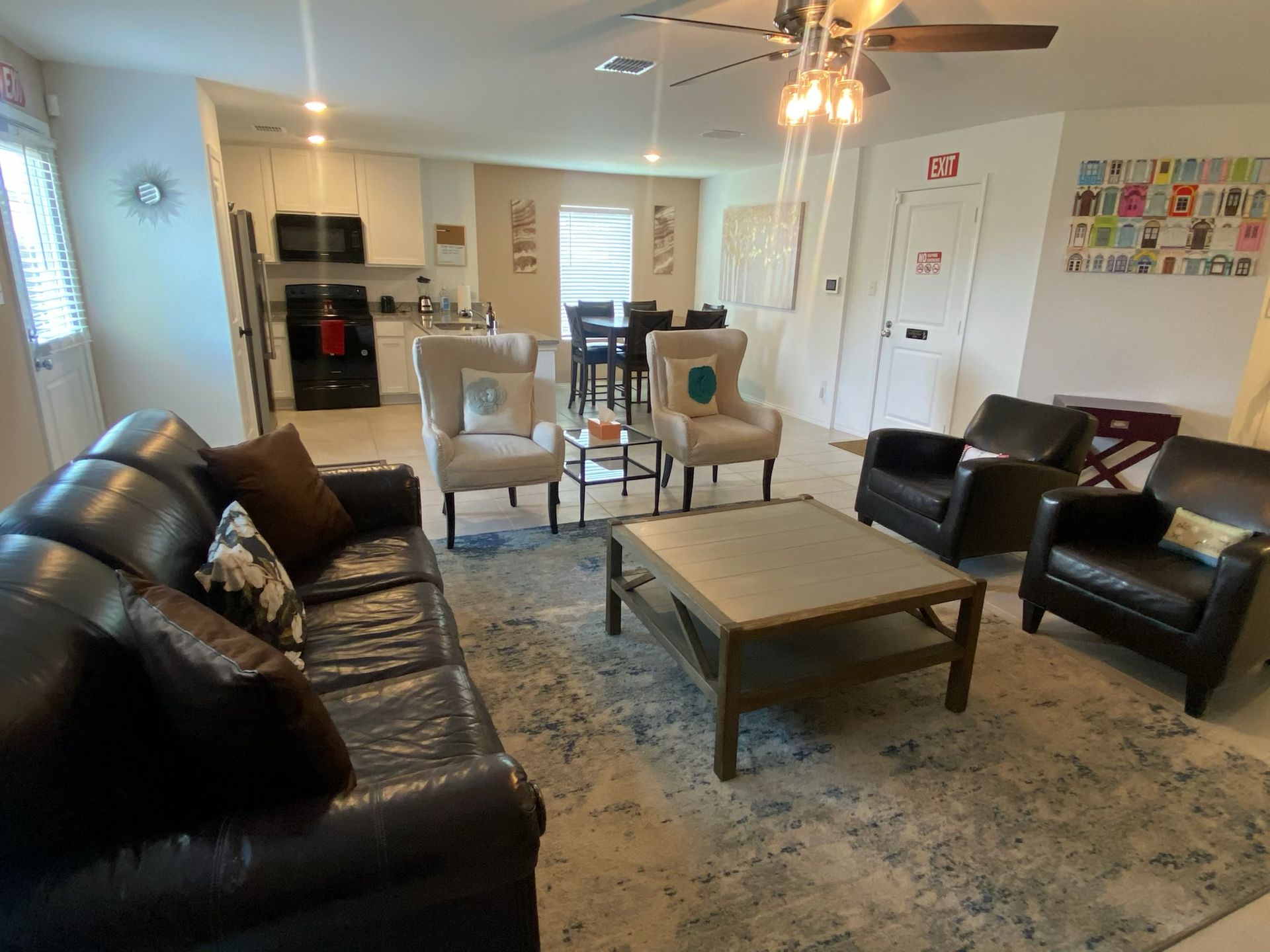 Living room with black leather sofas, armchairs, coffee table, and open kitchen beyond