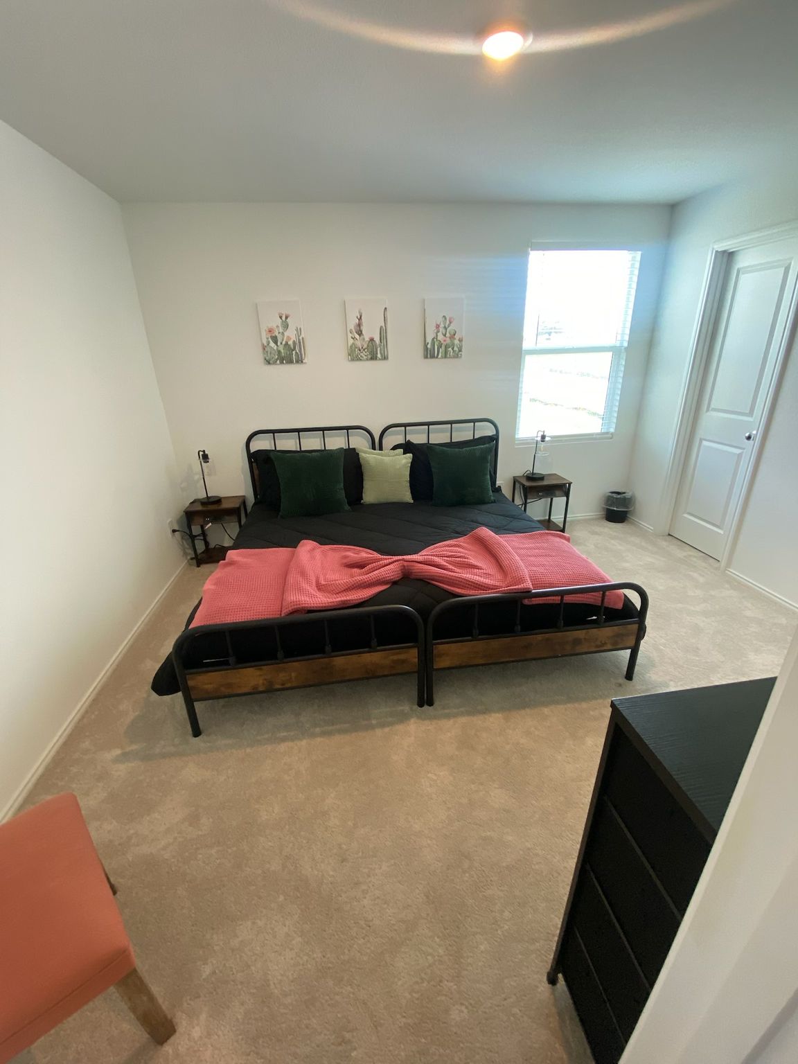 Small bedroom with two twin beds, beige carpet, white walls, and a window by a closet door.