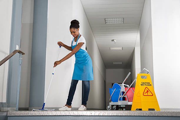Woman mopping a hallway with cleaning supplies, wearing a blue apron, and a 