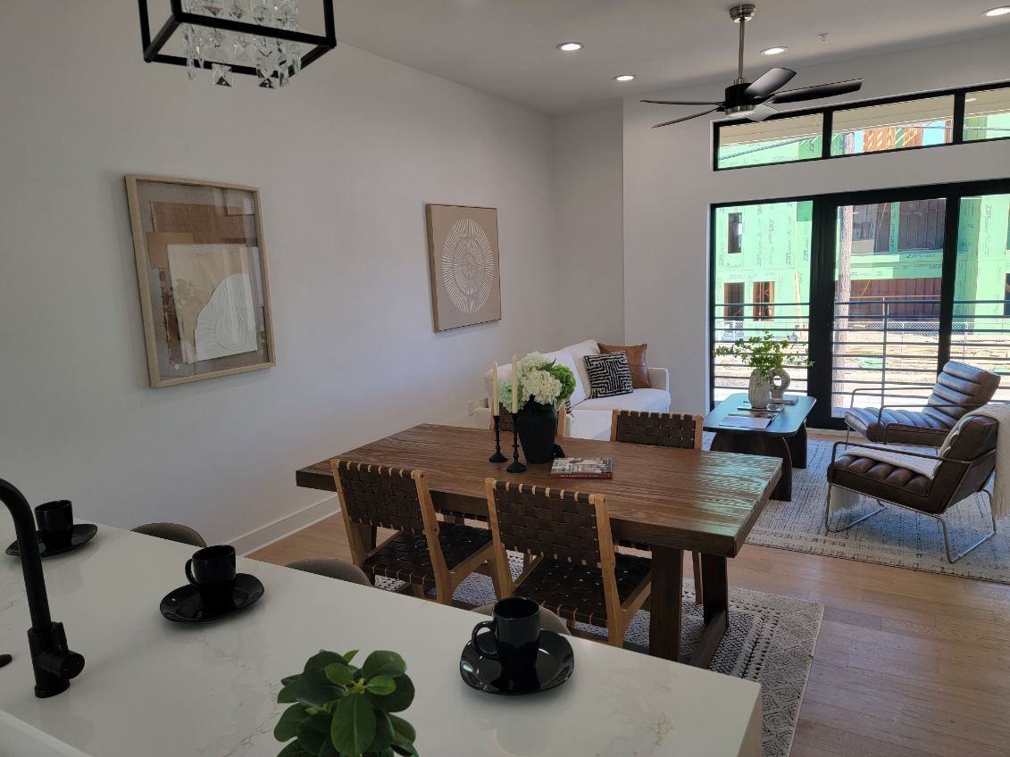 Dining and living area with wooden table, chairs, sofa, coffee table, and large windows.