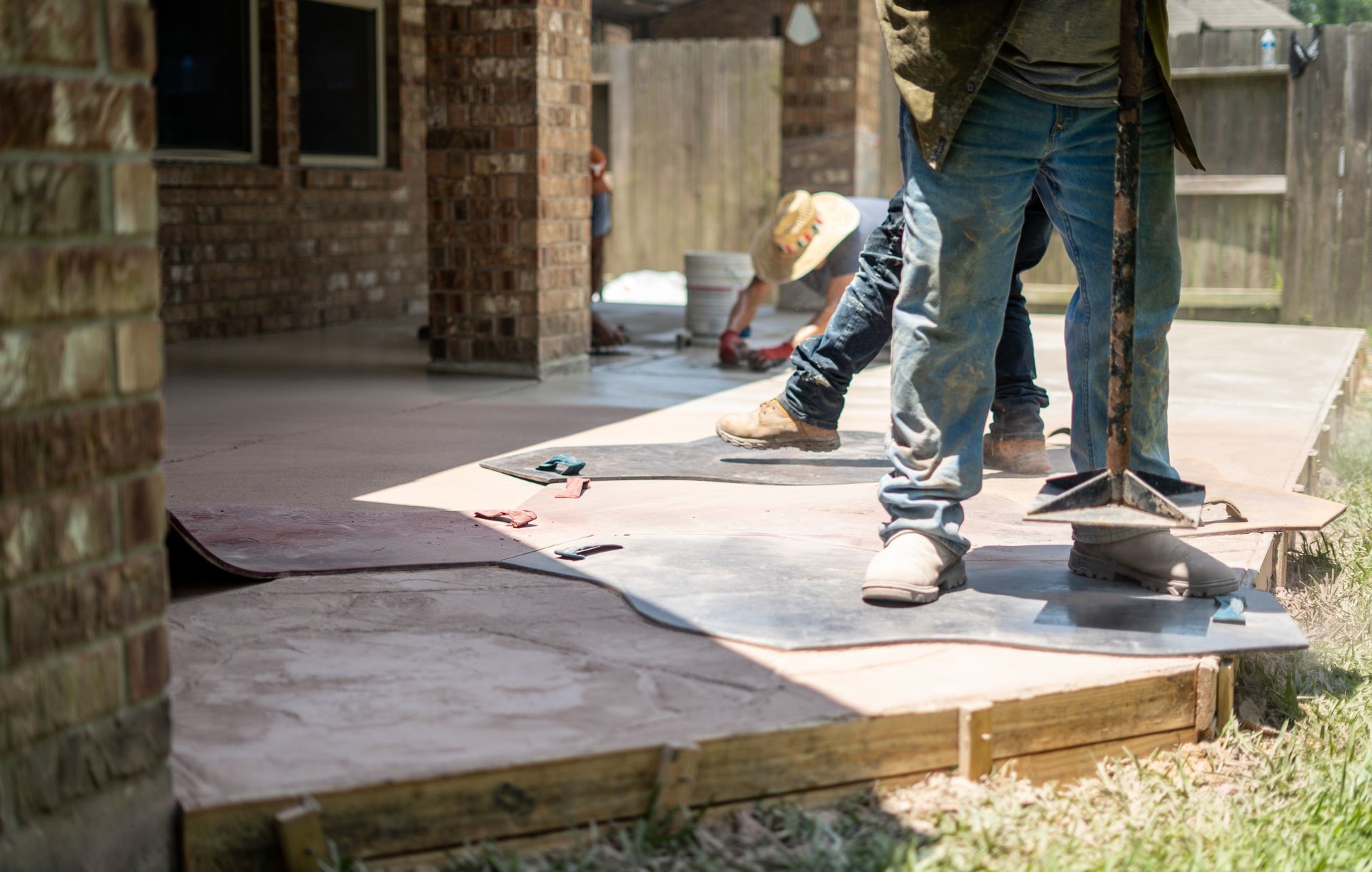 Workers pouring concrete on a patio with a brick building in the background.