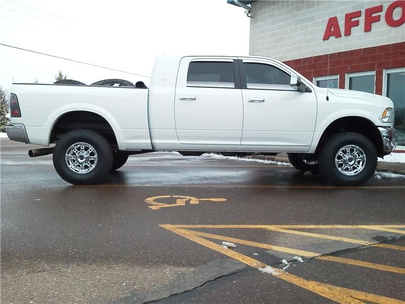 White lifted pickup truck parked outside a storefront on a wet lot.