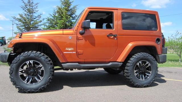 Orange Jeep Wrangler parked outdoors on a sunny day with large off-road tires