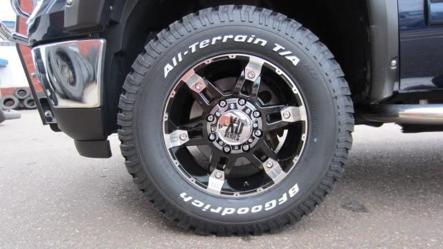 Close-up of a black off-road truck wheel with white lettering and chrome rim on pavement