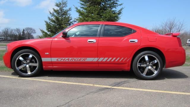 Red sports coupe parked in a lot, side view, with black racing stripes and chrome wheels