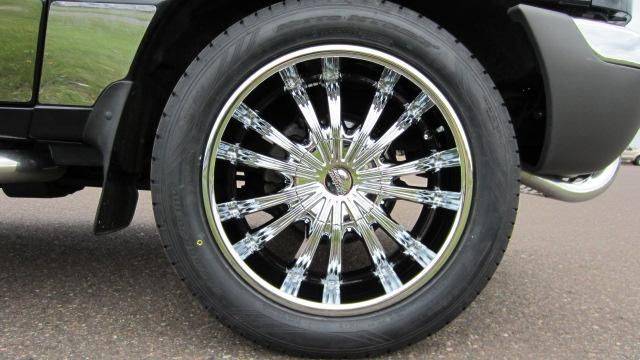 Close-up of a black truck’s chrome wheel and tire on a paved road.
