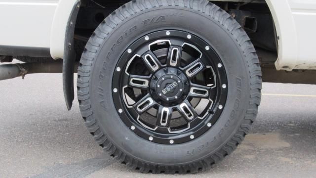 Black off-road truck wheel with rugged tire on a white vehicle, parked on pavement