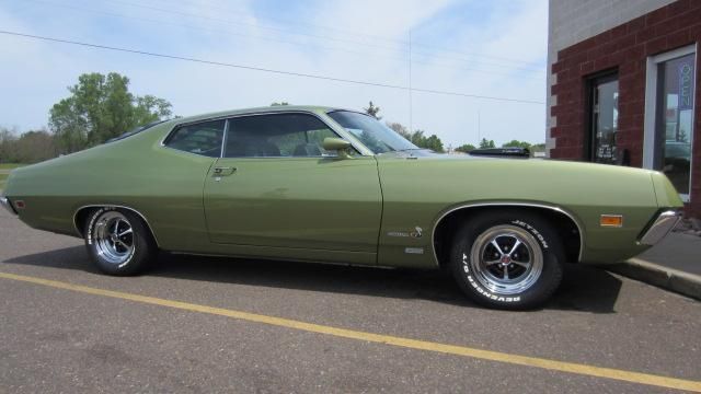 Green classic muscle car parked on a street beside a building