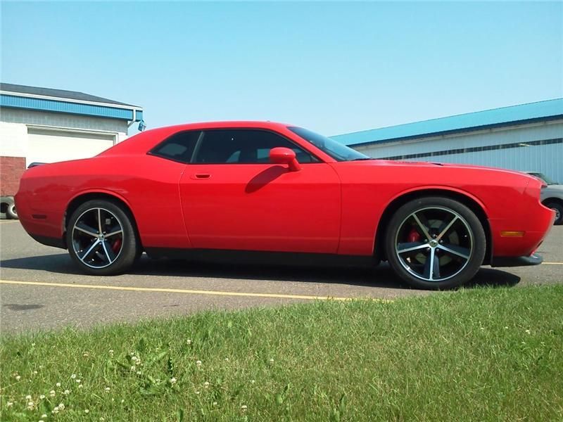 Red sports coupe parked outdoors on pavement beside grass, with a blue building in the background.